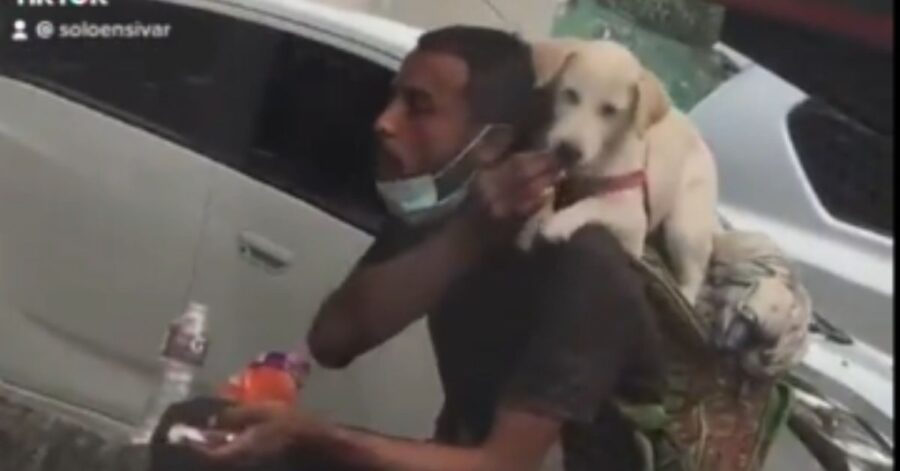 Un giovane senzatetto condivide il suo cibo con il cucciolo che porta sulla schiena