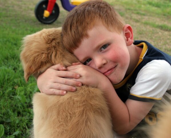 Bambino abbraccia un cane color caramello